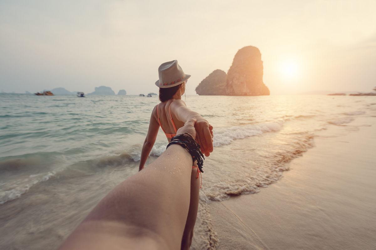 pov d'un homme tenant la main d'une femme. elle est debout dans la mer sur la plage de Railay, regardant vers les îles de Krabi.