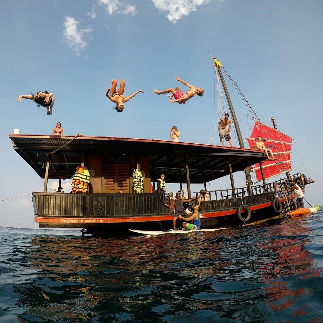 Croisières alcoolisées en Thaïlande - des gens font des saltos arrière sur le pont supérieur du bateau pirate Krabi Sunset Cruise, avec deux personnes sur un paddleboard à l'avant.