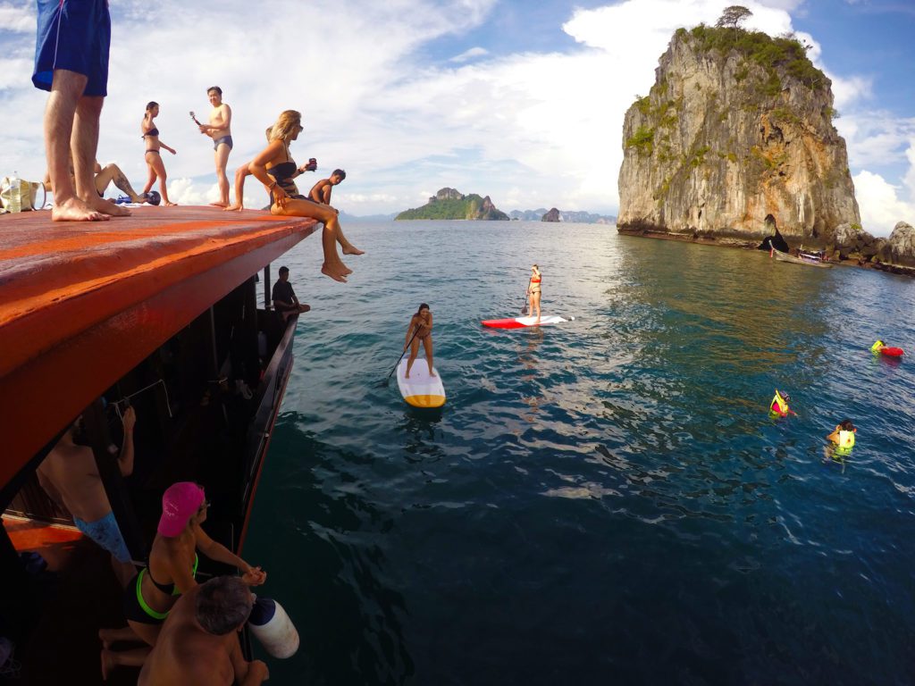 Invitados en el barco Krabi Sunset Cruise observando a la gente nadando y practicando paddleboarding en el mar con islas al fondo en Krabi.