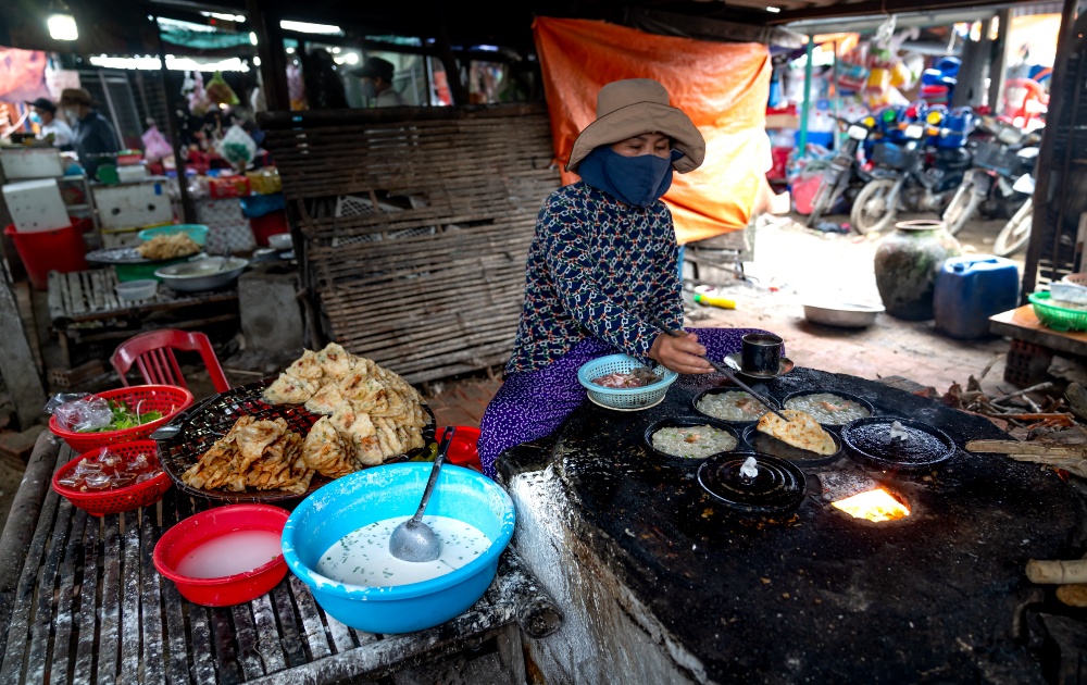 lady preparing local thai food on a large hot plate in a market