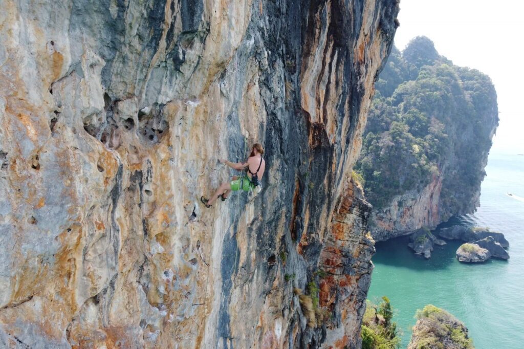 a rock climber in railay thailand, a flat cliff with sea and island views from their high point