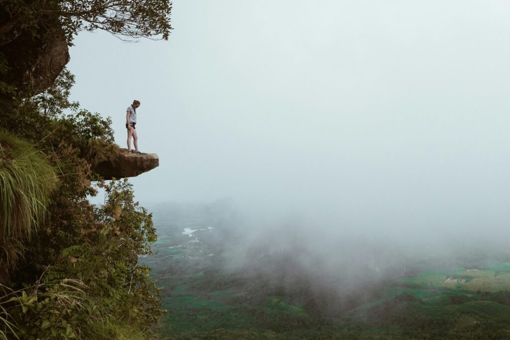 Une personne debout sur un rocher en saillie, surplombant la randonnée de la montagne Dragon Crest : point de vue Khao Ngon Nak avec un arrière-plan brumeux.
