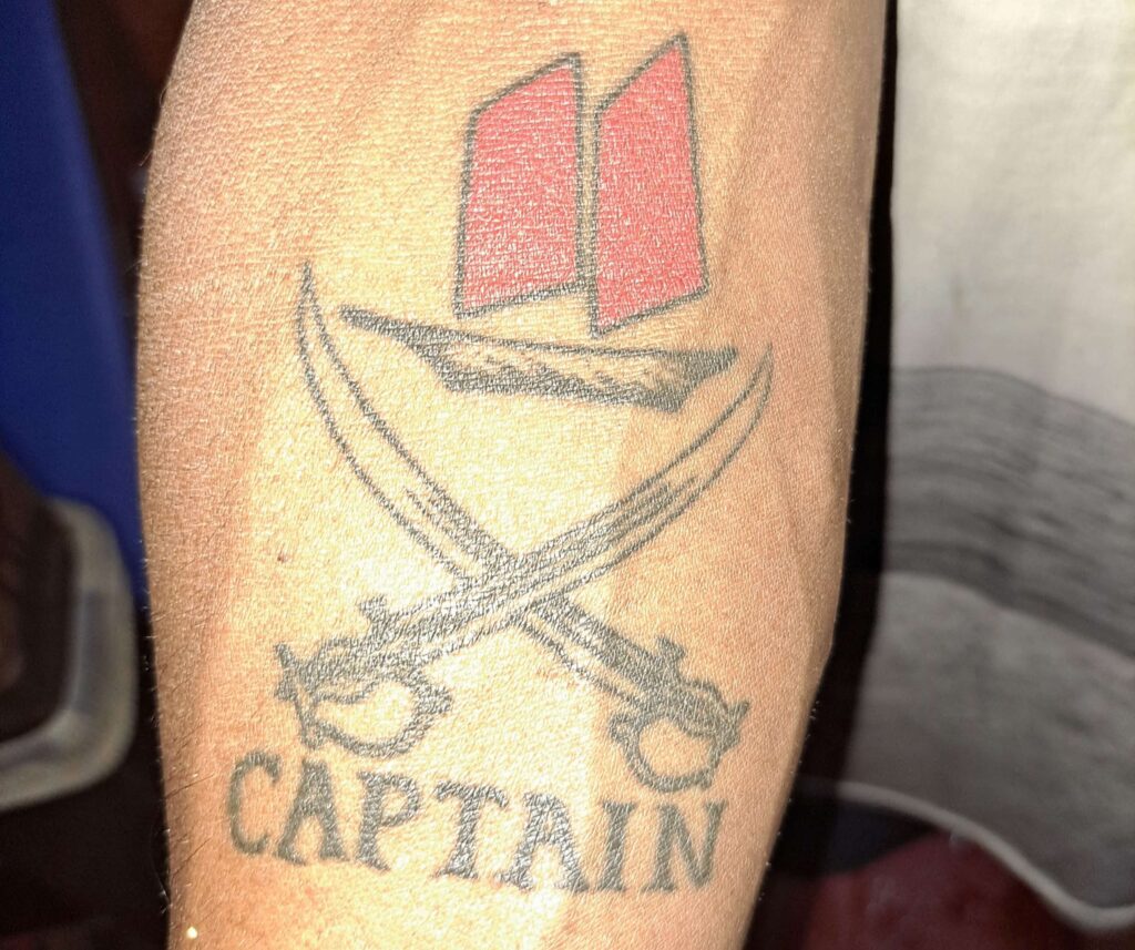 primer plano de un tatuaje krabi sunset tour con espadas cruzadas y la palabra captain debajo