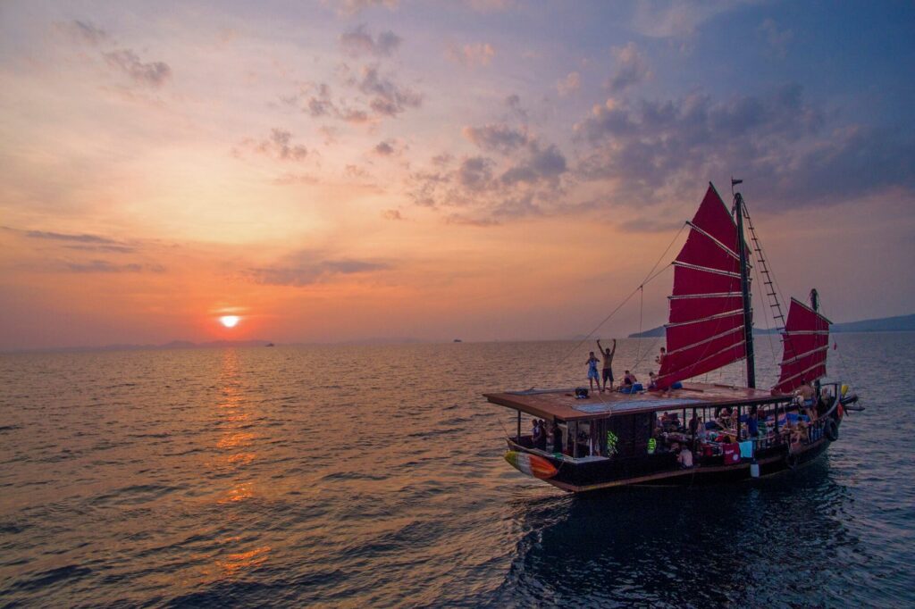 un barco junco tradicional en el mar con sus velas rojas al atardecer