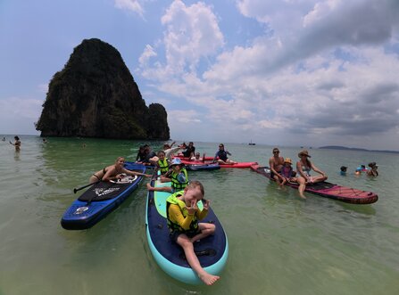 Group of adults and children relaxing on paddleboards near a limestone island at Railay Beach