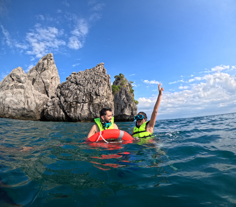 Dos buceadores con chaleco salvavidas flotando cerca de acantilados rocosos de piedra caliza en aguas cristalinas frente a Krabi.