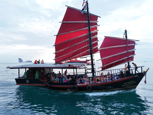 Traditional Thai junk boat with red sails cruising in the Andaman Sea with guests onboard