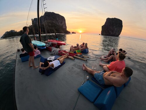 Guests relaxing on the roof of a junk boat with cushions, watching the sun set behind the islands