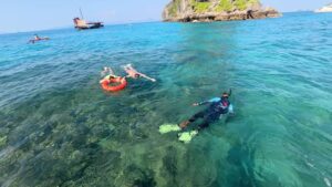 Un guide emmène deux personnes sur les récifs de Koh Ya Wa Sam à l'aide d'une bouée de sauvetage. Junk boat de Krabi Sunset Cruises en arrière-plan.