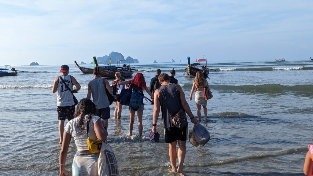 groups of people wading through the water at aonang beach to a longtail boat
