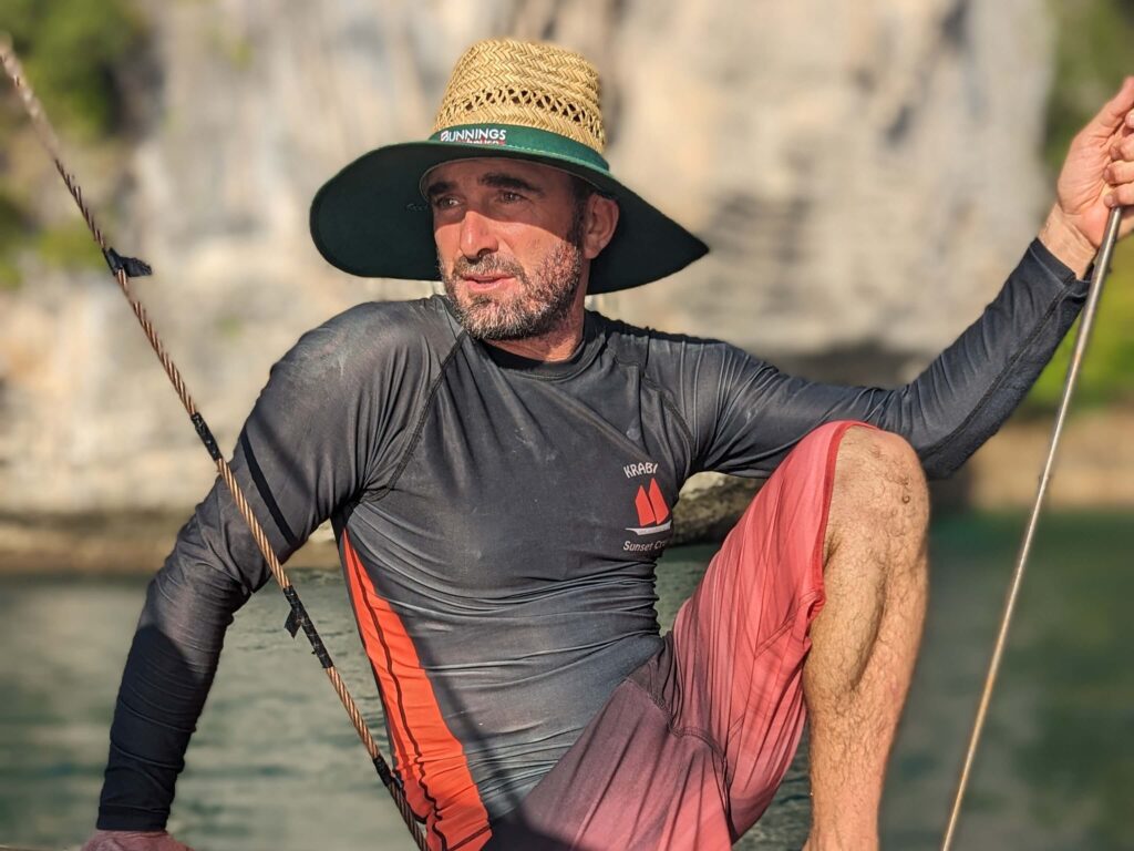 guide michael of krabi sunset cruises sitting on the side of the boat with cliffs in the background