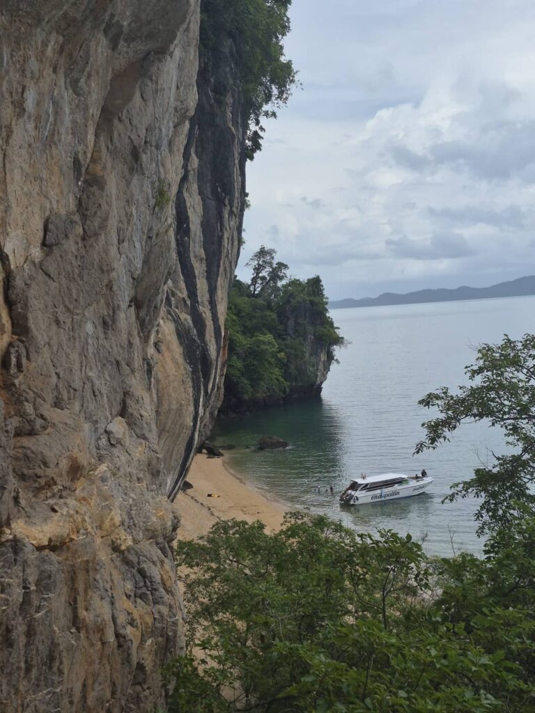 Un hors-bord amarré près d'une plage isolée, au pied de falaises calcaires, dans la baie de Phang Nga