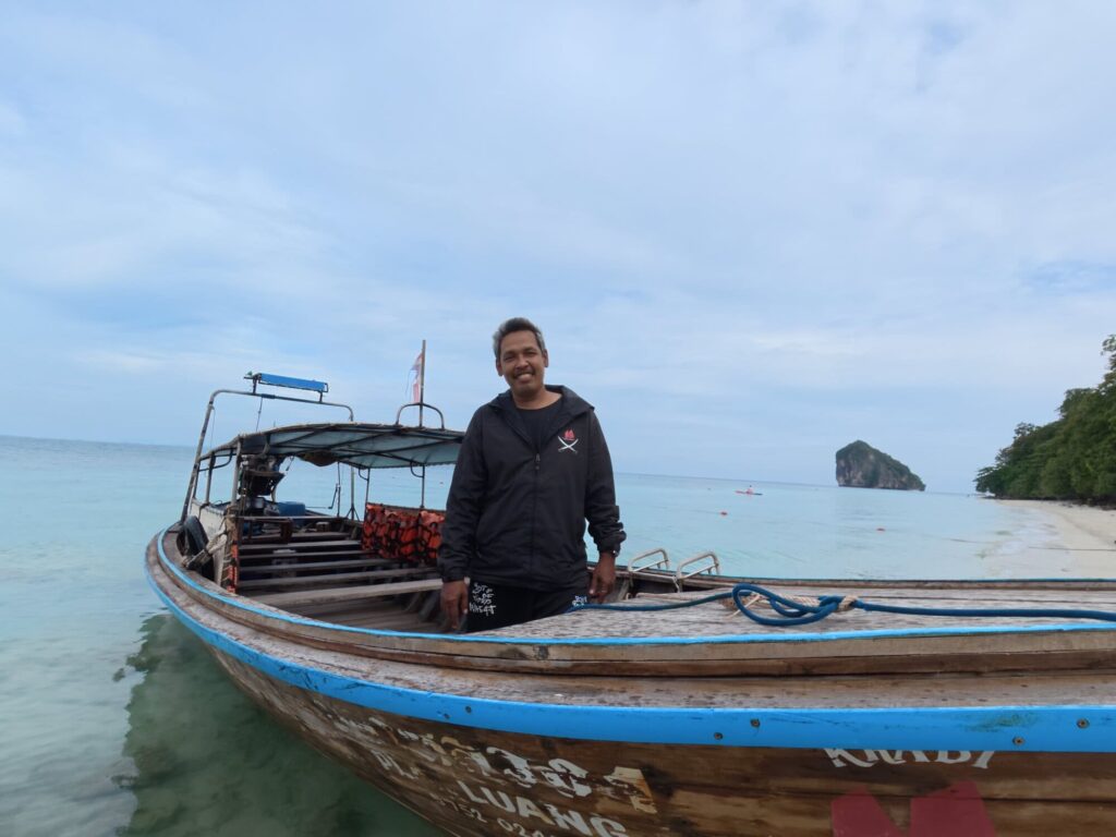 Lo, Krabi Sunset Cruises longtail boat driver, standing beside a traditional Thai longtail boat