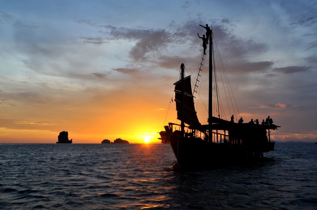 Junk boat at sunset in Krabi with 2 people climbing the mast