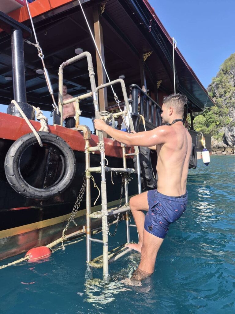 Un passager remonte à bord du bateau de Krabi Sunset Cruises en empruntant la grande échelle latérale depuis la mer