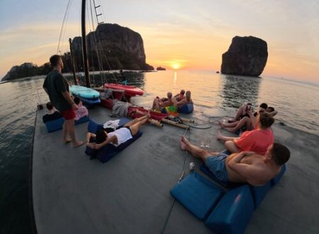 Guests relaxing on the roof of a junk boat with cushions, watching the sun set behind the islands
